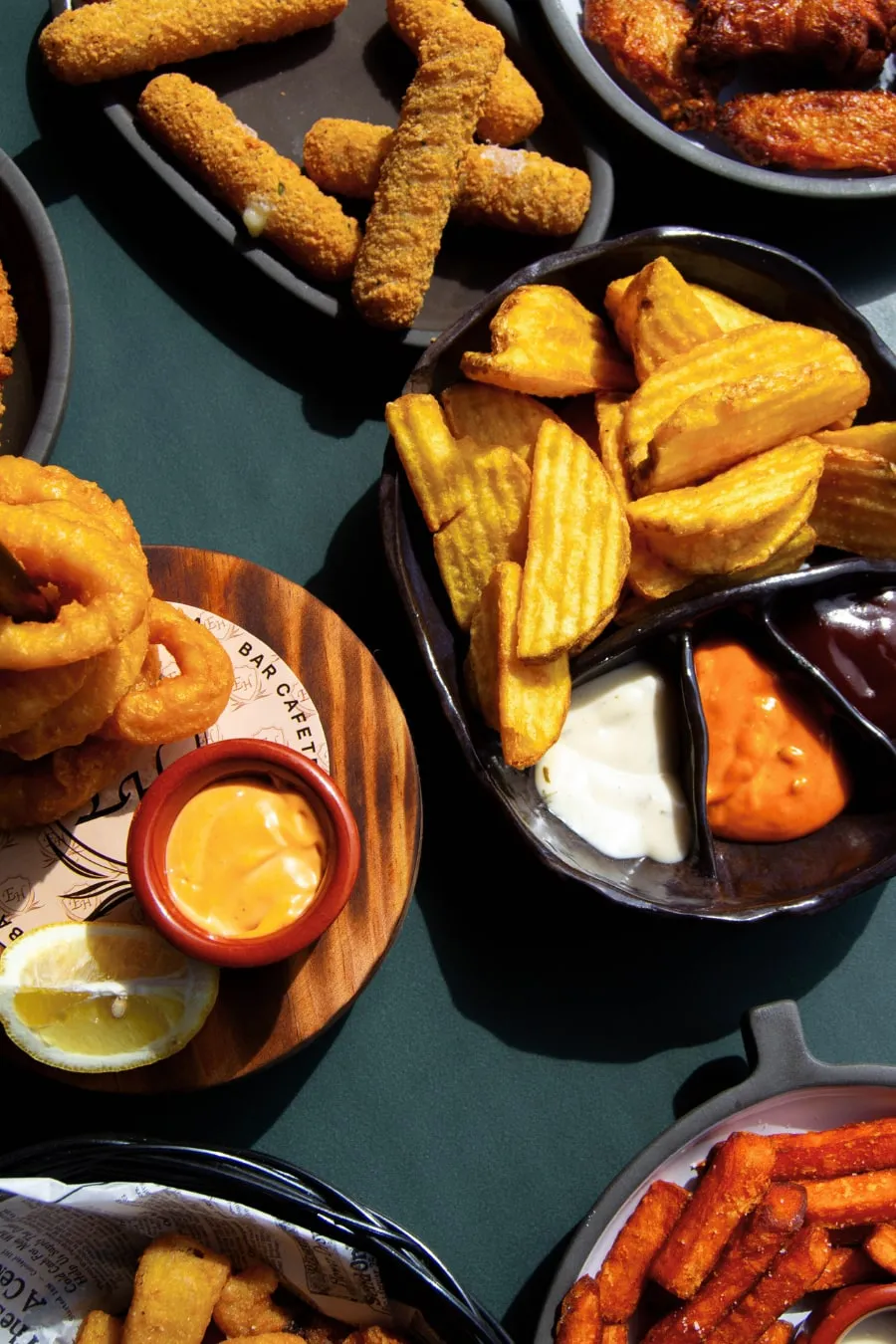 Mesa con tapas para compartir: aros de calamar, sticks de mozzarella, patatas, alitas y boniato frito con salsas.
