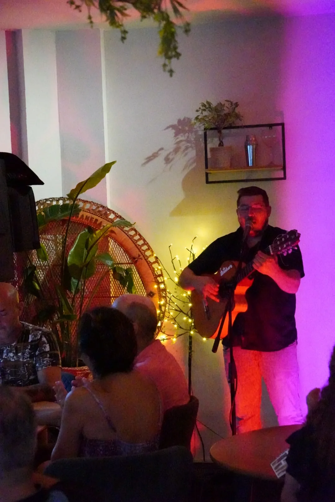 Un guitarrista actúa en el rincón del escenario, iluminado de violeta.