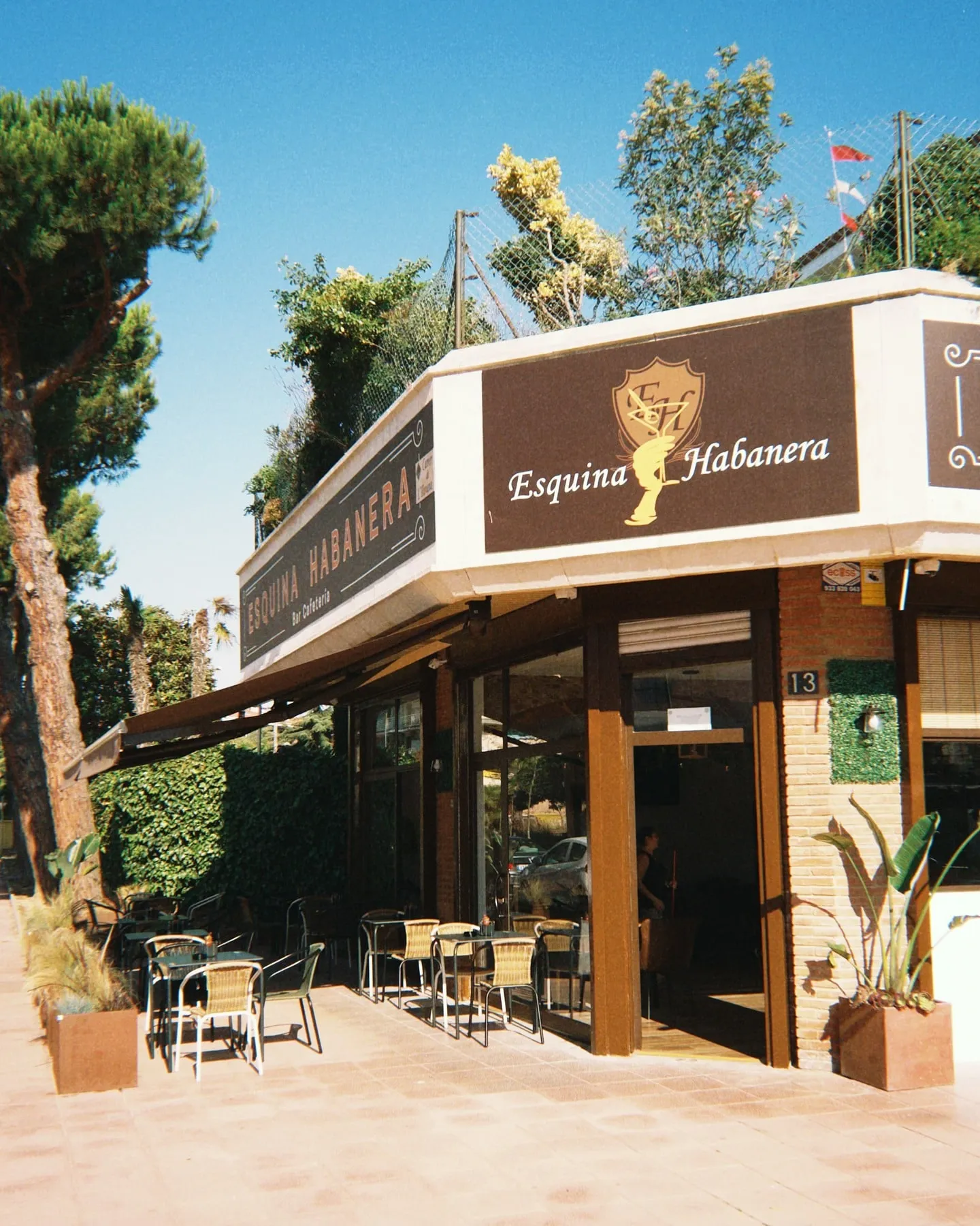 La esquina de Esquina Habanera: el rótulo sobre la fachada, la terraza con mesas y los pinos de Fenals.
